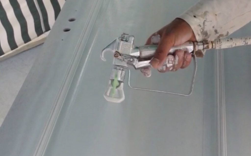 Spraydec hand holding spray gun spraying a wooden door in white satin paint